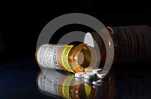 Macro of oxycodone opioid tablets with prescription bottles against dark background