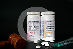 Oxycodone Hydrochloride prescription bottles isolated on black background with pills, gavel and syringes infront.