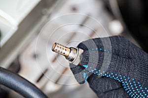 Oxygen sensor for gasoline and diesel engines in the hand against car engine. Mechanic holds oxygen sensor. lambda probe