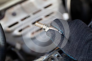 Oxygen sensor for gasoline and diesel engines in the hand against car engine. Mechanic holds oxygen sensor. lambda probe