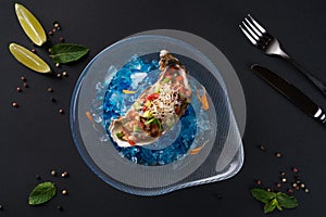 Oyster tartare. Fish delicacy on blue ice. Beautiful serving of seafood on a black background