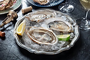 Oysters on ice at a restaurant, with lemon, lime, and white wine, on black