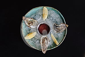 Oysters, served chilled with red wine cocktail sauce and fresh lemon on black wooden background, top view