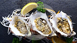 Oysters in Shells Fried with Garlic and Lemon on Black Textured Slate Background