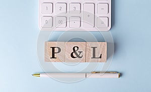 P AND L word on wooden block with pen and calculator on blue background