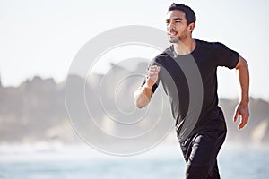 Pace yourself. a handsome young male athlete out for a run on the beach.