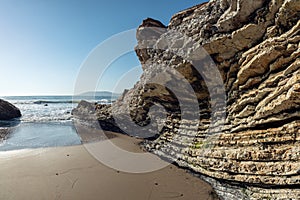 A Pacific coastline with yellow sandstone cliffs and waves rushing the beach.