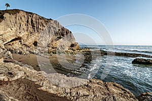 A Pacific coastline with yellow sandstone cliffs and waves rushing the beach.