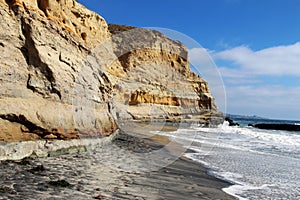 A Pacific coastline with yellow sandstone cliffs and waves rushing the beach