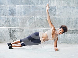 Pacific islander athlete girl with afro performing exercising routines plank with twist, one hand raised