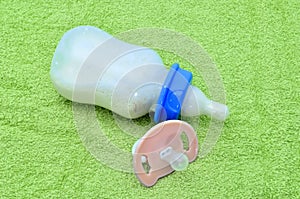 Pacifier and baby bottle with milk for a baby on green towel