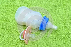 Pacifier and baby bottle with milk for a baby on green towel