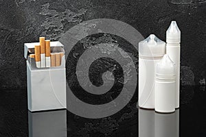 Pack of cigarettes and e-juice liquid bottles on black background