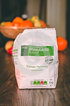 Pack of sugar on top of a wooden table with healthy fruit in the background