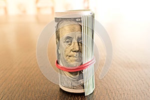 A pack of twisted 100 dollar bills . On a wooden table. Close up