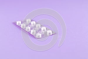 Pack of white pills packed in blister with copy space on purple background. Focus on foreground, soft bokeh