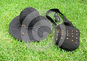 Packable black wide-brim sun hat, crochet bag and sunglasses on green grass photo
