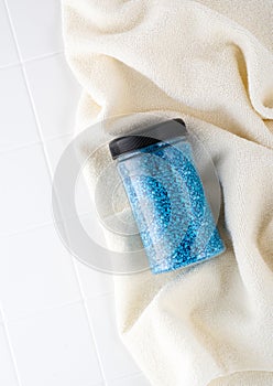 Package of blue glitter crystal salt on a bathroom beige towel. Jar of shimmering blue sea salt for home spa. Idea of relaxation,