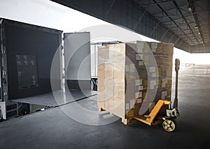 Package Boxes with Hand Pallet Truck Load into Cargo Container. Truck Parked Loading at Dock Warehouse. Delivery Service.