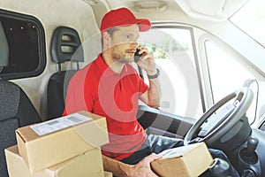 Package delivering - delivery man using mobile phone while sitting in van