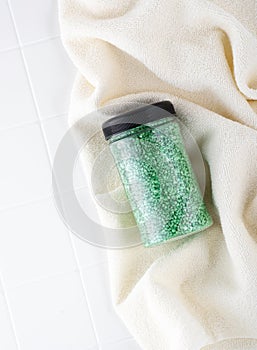Package of green glitter crystal salt on a bathroom beige towel. Jar of shimmering green sea salt for home spa. Idea of relaxation