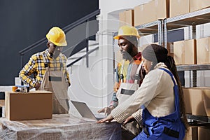 Package handlers packing parcel, checking orders list on laptop