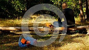 A package with plastic garbage lies on a glade, a fire burns, people walk in the background, camping and nature