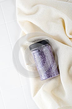 Package of purple shiny crystal salt on a bathroom beige towel. Jar of shimmering purple sea salt for home spa. Idea of relaxation