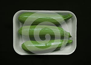 Packaged 3 three fresh whole green zucchini in white plastic tray and wrapped in cling film. Clipping path. isolated on black