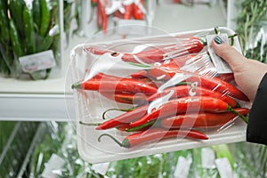 Packaged chili peppers with woman hand in the supermarket