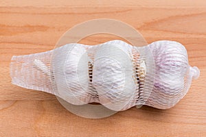 Packaged white garlic bulbs in net place on wooden table, genera
