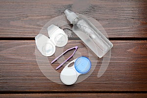 Packages with contact lenses, case, tweezers and drops on wooden table, flat lay