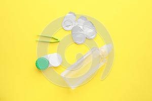 Packages with contact lenses, case, tweezers and drops on yellow background, flat lay