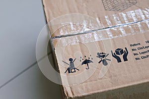 Packaging symbol on a brown cardboard parcel box, do not sit on the box, keep dry with umbrella and Rain sign, do not step, handle