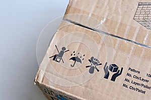 Packaging symbol on a brown cardboard parcel box, do not sit on the box, keep dry with umbrella and Rain sign, do not step, handle