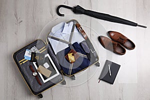 Packed suitcase with business trip stuff on wooden surface, flat lay