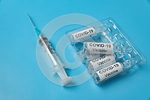 Packing of ampoules with vaccine COVID-19 and syringe. Blue background. Medical concept