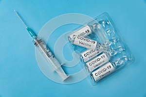 Packing of ampoules with vaccine COVID-19 and syringe on a blue background. Medical concept