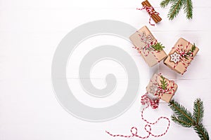 Packing Christmas gifts. Eco craft holidays gift boxes tied with red and white string , decorations, pine branches on white table.