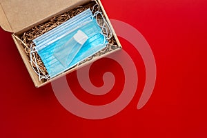 Packing a Christmas present during Coronavirus epidemic. Face masks and hydroalcoholic gel inside a cardboard box on a red