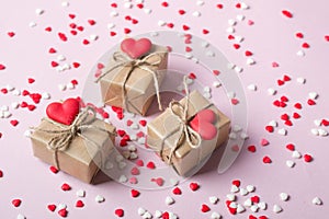 Packing gifts in vintage beige craft paper and red sweet sugar candy hearts. On pink background with sprinkles.