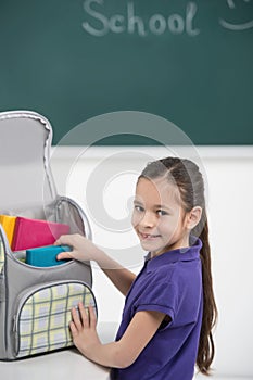 Packing her book bag. Cheerful little schoolgirl packing her boo