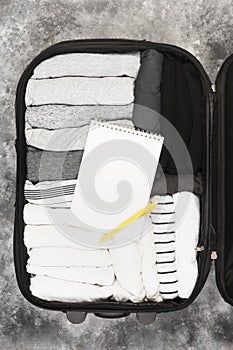 Packing of monochrome clothes in black suitcase. Packing list in