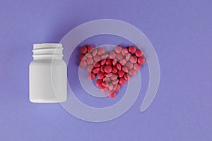 Packing pills. Heart shape made of pills. Pills spilling out of a jar on a purple background
