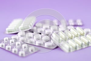 Packs of white capsules and pills packed in blisters with copy space on purple background. Focus on foreground, soft bokeh
