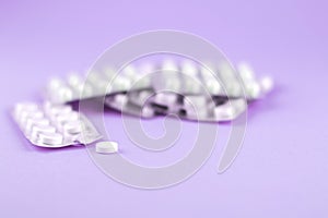 Packs of white capsules and pills packed in blisters with copy space on purple background. Focus on foreground, soft bokeh