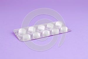 Packs of white pills packed in blisters with copy space on purple background. Focus on foreground, soft bokeh