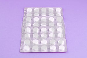 Packs of white pills packed in blisters with copy space on purple background. Focus on foreground, soft bokeh