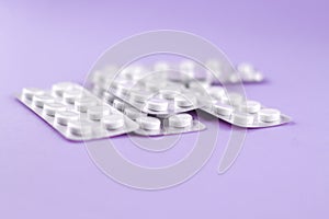 Packs of white pills packed in blisters with copy space on purple background. Focus on foreground, soft bokeh