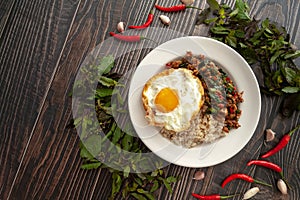 Pad Kra Pao Moo Sab with Kai Dao on wooden backgound, Thai famous food, the stir-fried minced pork, garlic, basil and chili topped